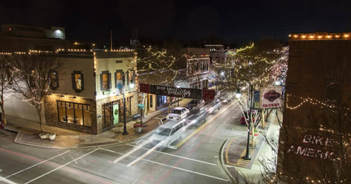 A bustling street at night, adorned with festive lights and holiday decorations, showcasing shops and traffic.