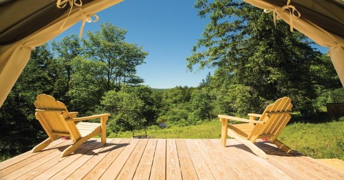 Two wooden chairs on a deck overlook a lush green landscape and a clear blue sky.