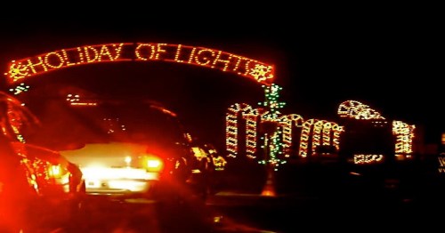 A festive archway reading "Holiday of Light" adorned with colorful lights, set against a dark night sky.
