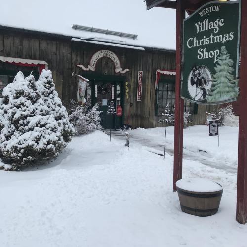 A snowy scene featuring a rustic Christmas shop with festive decorations and a sign in front.