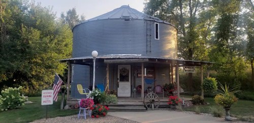 A round, metal silo converted into a charming hotel, surrounded by flowers and greenery.