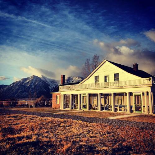 A historic house with a porch, set against a backdrop of snow-capped mountains and a dramatic sky.