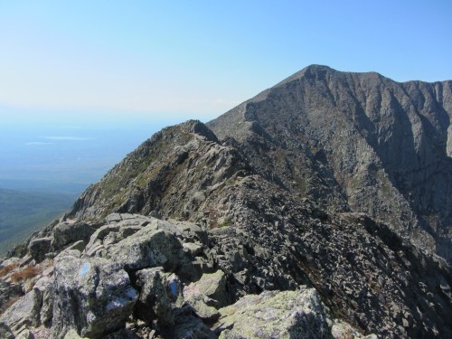 A rocky mountain ridge with a clear blue sky and distant peaks visible in the background.