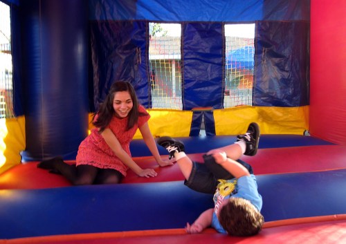 A woman laughs as a child playfully tumbles in a colorful bounce house.