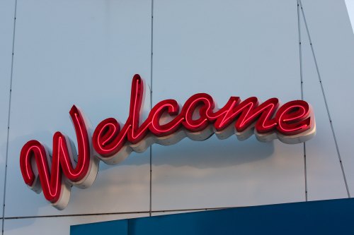 A bright red neon sign that reads "Welcome" against a white background.
