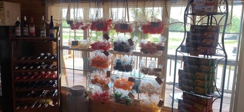 A cozy shop interior featuring wine bottles, colorful candy baskets, and a display of Breton crackers by a sunny window.