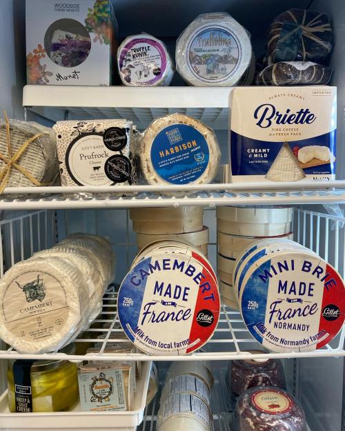 A refrigerator shelf filled with various cheeses, including Camembert and Brie, alongside decorative packaging.