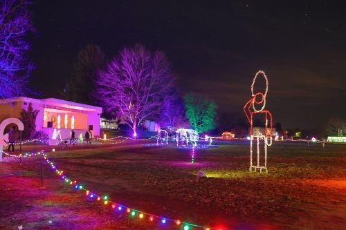 Colorful holiday lights illuminate a park at night, featuring festive displays and a large light figure.