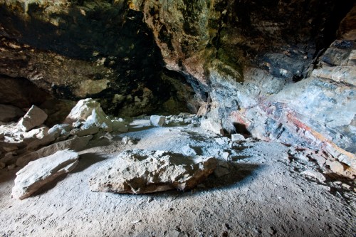 A dimly lit cave interior with rocky surfaces and scattered boulders on the ground.