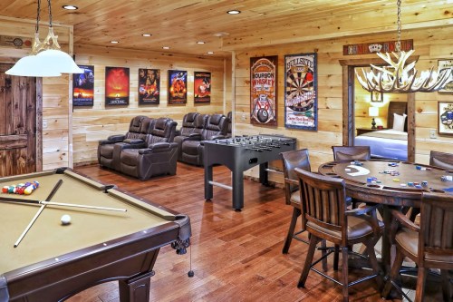 A cozy game room featuring a pool table, foosball table, poker table, and comfortable seating with wooden walls.