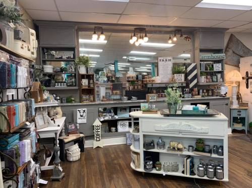 A cozy shop interior featuring shelves of home decor, gifts, and a coffee station, with warm lighting and wooden floors.