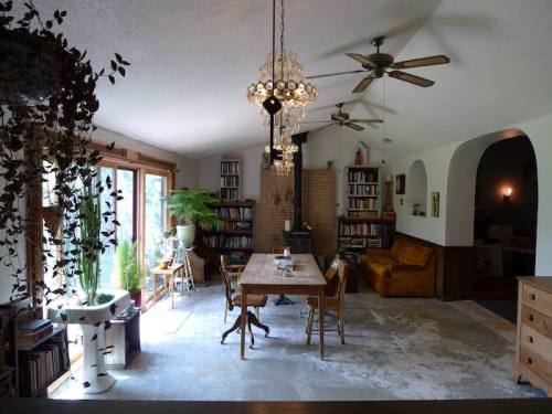 Cozy dining area with a wooden table, bookshelves, plants, and a chandelier, featuring a warm, inviting atmosphere.