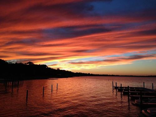 A vibrant sunset over a calm lake, with colorful clouds reflecting on the water and silhouettes of dock posts.