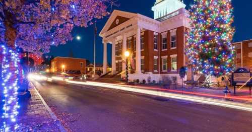 A festive street scene at night featuring a decorated Christmas tree and a historic building illuminated with lights.