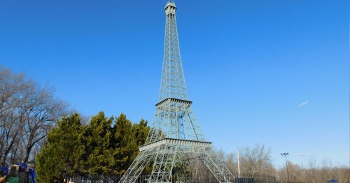 A miniature replica of the Eiffel Tower against a clear blue sky, surrounded by trees.