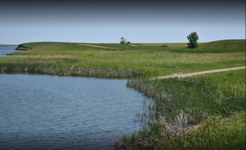 A serene landscape featuring a calm water body, grassy banks, and a clear blue sky.