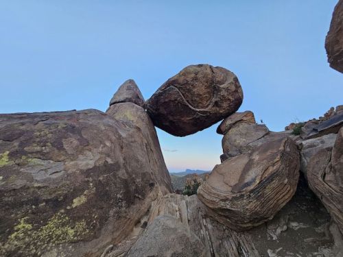 A large boulder balanced on top of two rock formations against a clear blue sky.