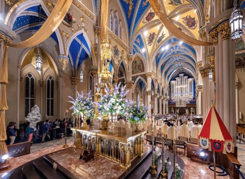 A beautifully decorated church interior with ornate architecture, floral arrangements, and a gathering of people.