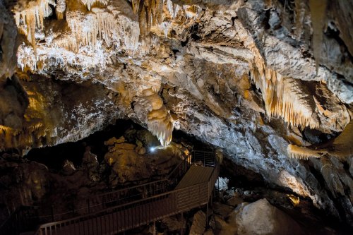 A dimly lit cave interior featuring stalactites and a metal walkway leading deeper into the cavern.
