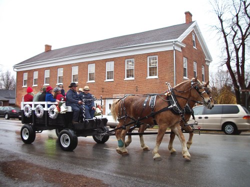 A horse-drawn carriage with passengers rides down a rainy street in front of a brick building.
