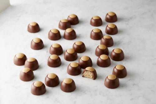 A variety of chocolate candies with a golden top, arranged on a marble surface, one candy partially bitten.