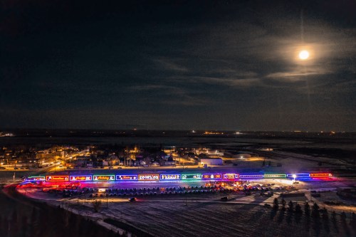 Aerial view of a brightly lit holiday display at night, with a full moon and snow-covered ground.