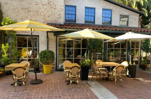 Outdoor dining area with yellow umbrellas, potted plants, and brick flooring beside a charming building.