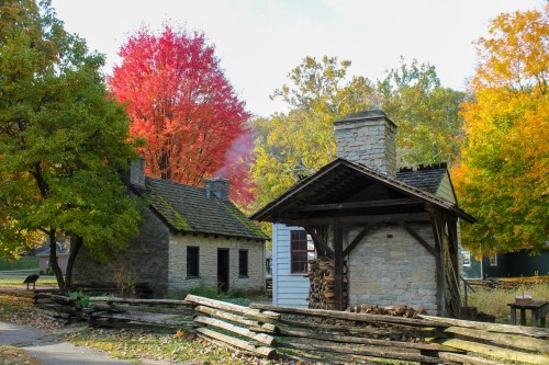 A scenic view of stone houses surrounded by vibrant autumn trees and a wooden fence.