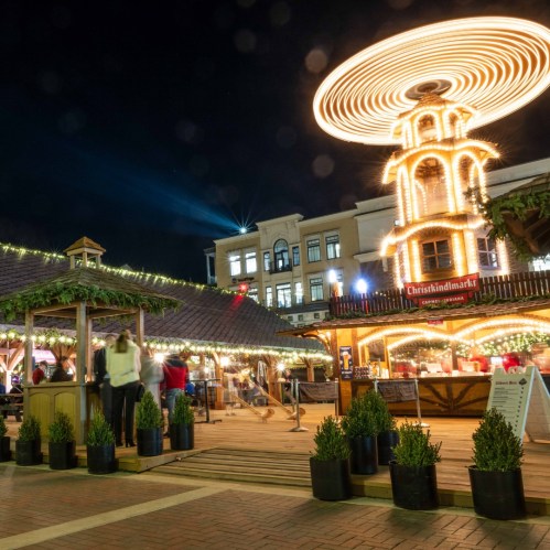 A festive market at night with a spinning carousel, twinkling lights, and people enjoying the holiday atmosphere.