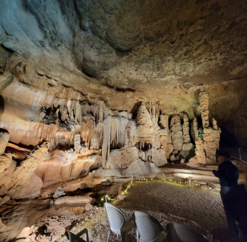 A dimly lit cave interior featuring unique rock formations and a small seating area with lights along the ground.
