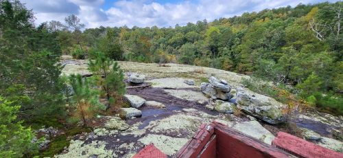 A scenic view of a rocky landscape covered in green moss, surrounded by trees under a partly cloudy sky.