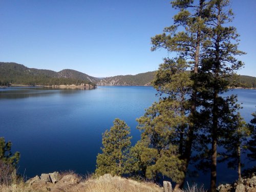 A serene lake surrounded by mountains and pine trees under a clear blue sky.