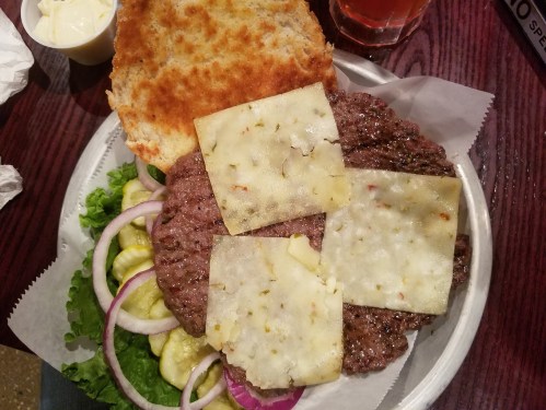 A plate with a burger featuring two beef patties, lettuce, pickles, onions, and melted cheese on a toasted bun.