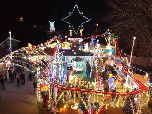 A brightly lit house decorated with colorful Christmas lights and festive figures, surrounded by people enjoying the display.