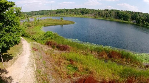 A serene lake surrounded by lush greenery and colorful vegetation under a clear blue sky.