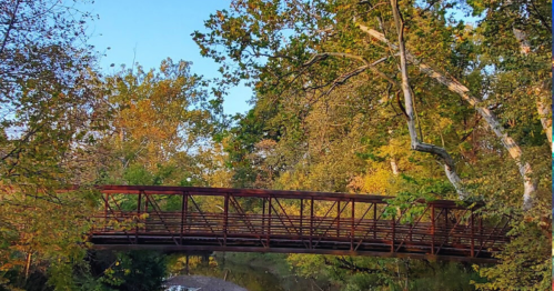 A rustic metal bridge surrounded by vibrant autumn trees and a clear blue sky.