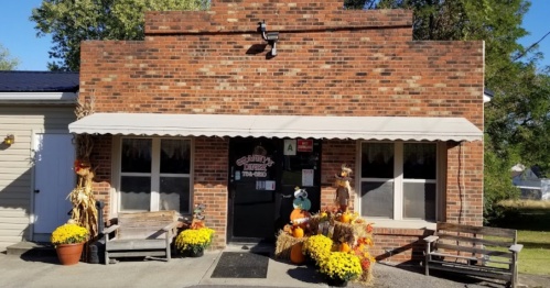 A brick building with a welcoming entrance, decorated with fall flowers and scarecrows.