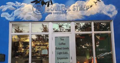 A blue storefront with "Soulful Steep Tea Company" sign, featuring large windows and a mural of clouds above.