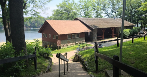 A wooden cabin by a lake, surrounded by trees, with a pathway leading down to the water.