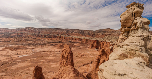 A panoramic view of rugged red rock formations and cliffs under a cloudy sky in a desert landscape.