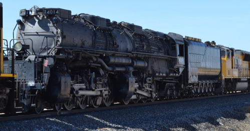 A vintage steam locomotive, Union Pacific 4014, stands on the tracks under a clear blue sky.