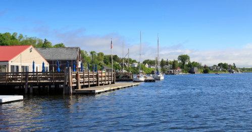 A serene waterfront scene with docks, sailboats, and lush greenery under a clear blue sky.