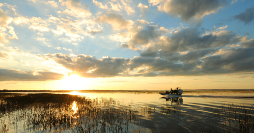A boat glides through calm waters at sunset, with clouds reflecting golden light over the landscape.