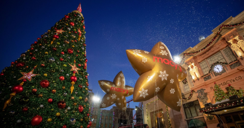 A festive scene featuring a decorated Christmas tree and large gold star balloons with "Macy's" in a holiday setting.