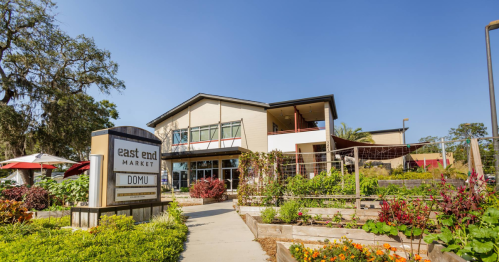 A modern market building with a sign for "East End Market" and vibrant gardens in the foreground.