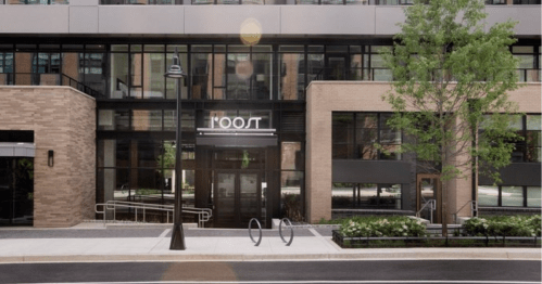 Modern building entrance with large glass windows, a sign reading "ROOT," and landscaped greenery.