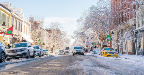 A snowy street lined with cars and festive decorations, showcasing a winter scene in a charming town.