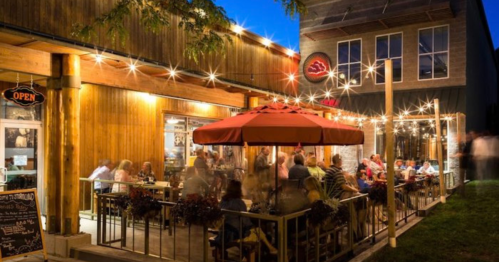 Outdoor dining area at night, with string lights and an umbrella, filled with people enjoying their meals.
