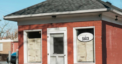 A small red brick building with a sign reading "The Shack" and boarded-up windows.