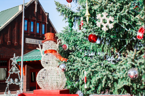 A festive scene featuring a decorated Christmas tree and a sparkling snowman in front of a brick building.